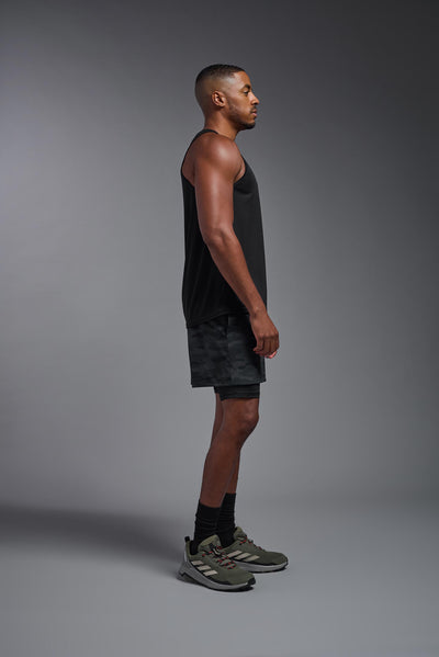 An African American male model with a beard on a gray background, wearing the Men's DriMax Endurance Tank in the color black from a full body side view. This shirt is made in the USA and is quick-drying and moisture-wicking. #color_black