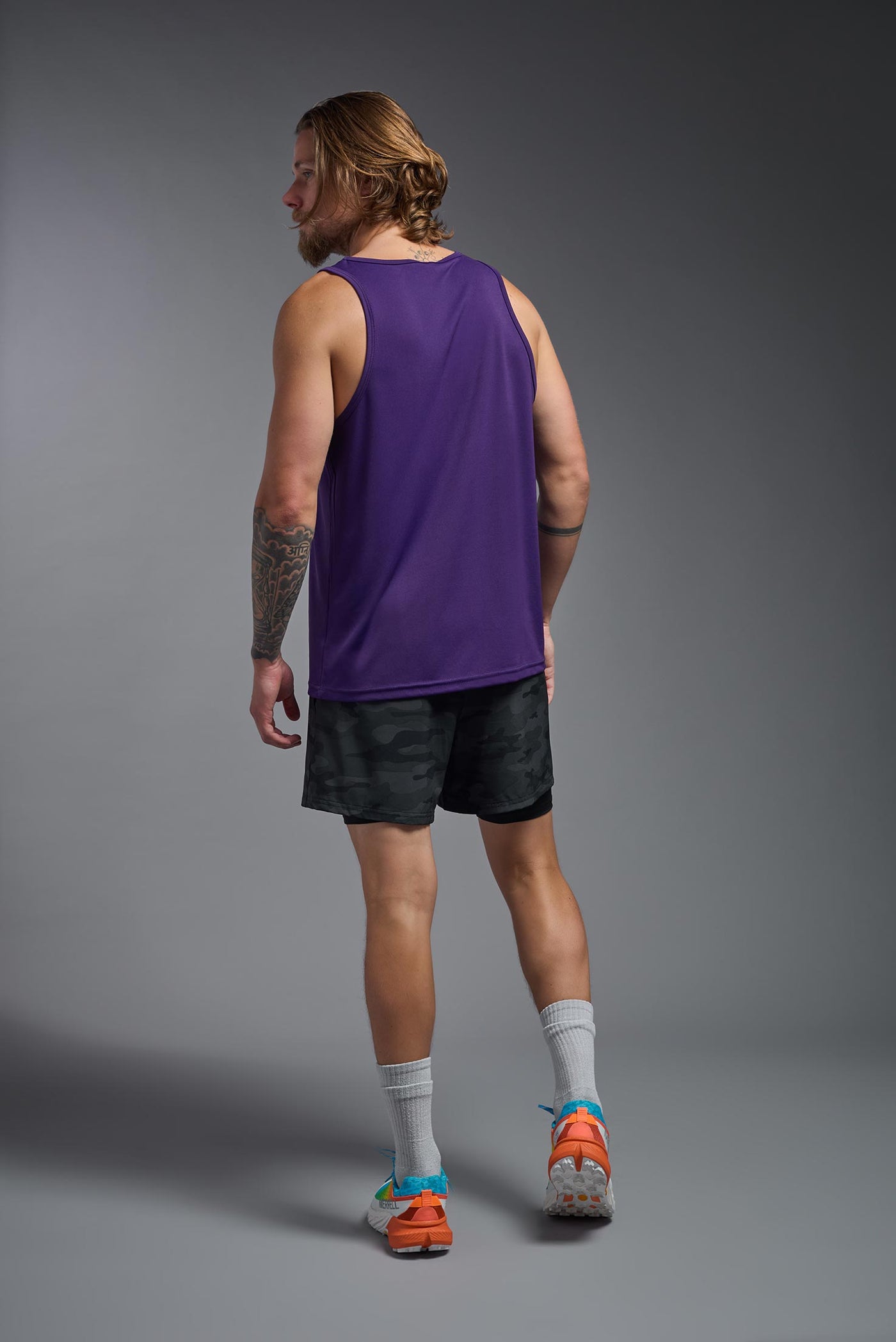 A blonde male model with a beard on a gray background, wearing the Men's DriMax Endurance Tank in the color dark purple from a full body back view. This shirt is made in the USA and is quick-drying and moisture-wicking. #color_dark-purple
