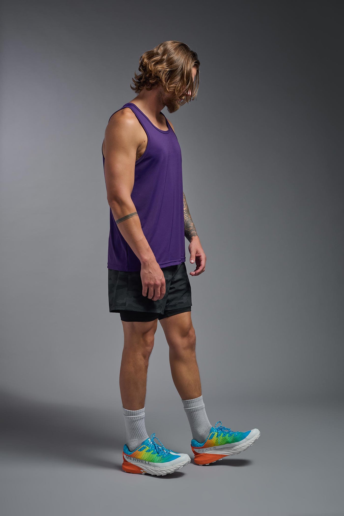 A blonde male model with a beard on a gray background, wearing the Men's DriMax Endurance Tank in the color dark purple from a full body side view. This shirt is made in the USA and is quick-drying and moisture-wicking. #color_dark-purple