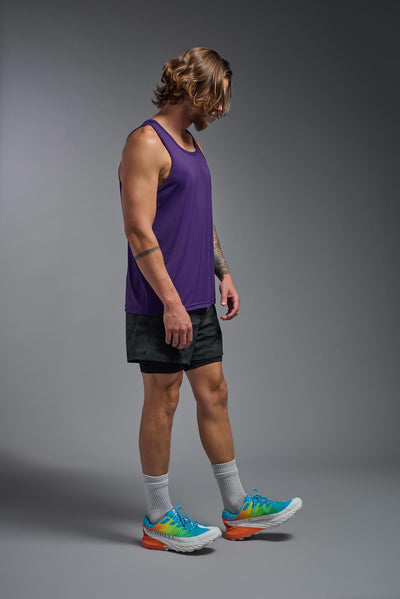 A blonde male model with a beard on a gray background, wearing the Men's DriMax Endurance Tank in the color dark purple from a full body side view. This shirt is made in the USA and is quick-drying and moisture-wicking. #color_dark-purple