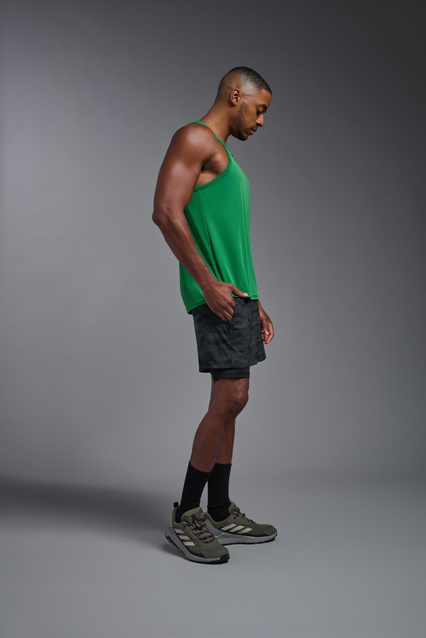 An African American male model with a beard on a gray background, wearing the Men's DriMax Endurance Tank in the color kelly green from a full body side view. This shirt is made in the USA and is quick-drying and moisture-wicking. #color_kelly-green
