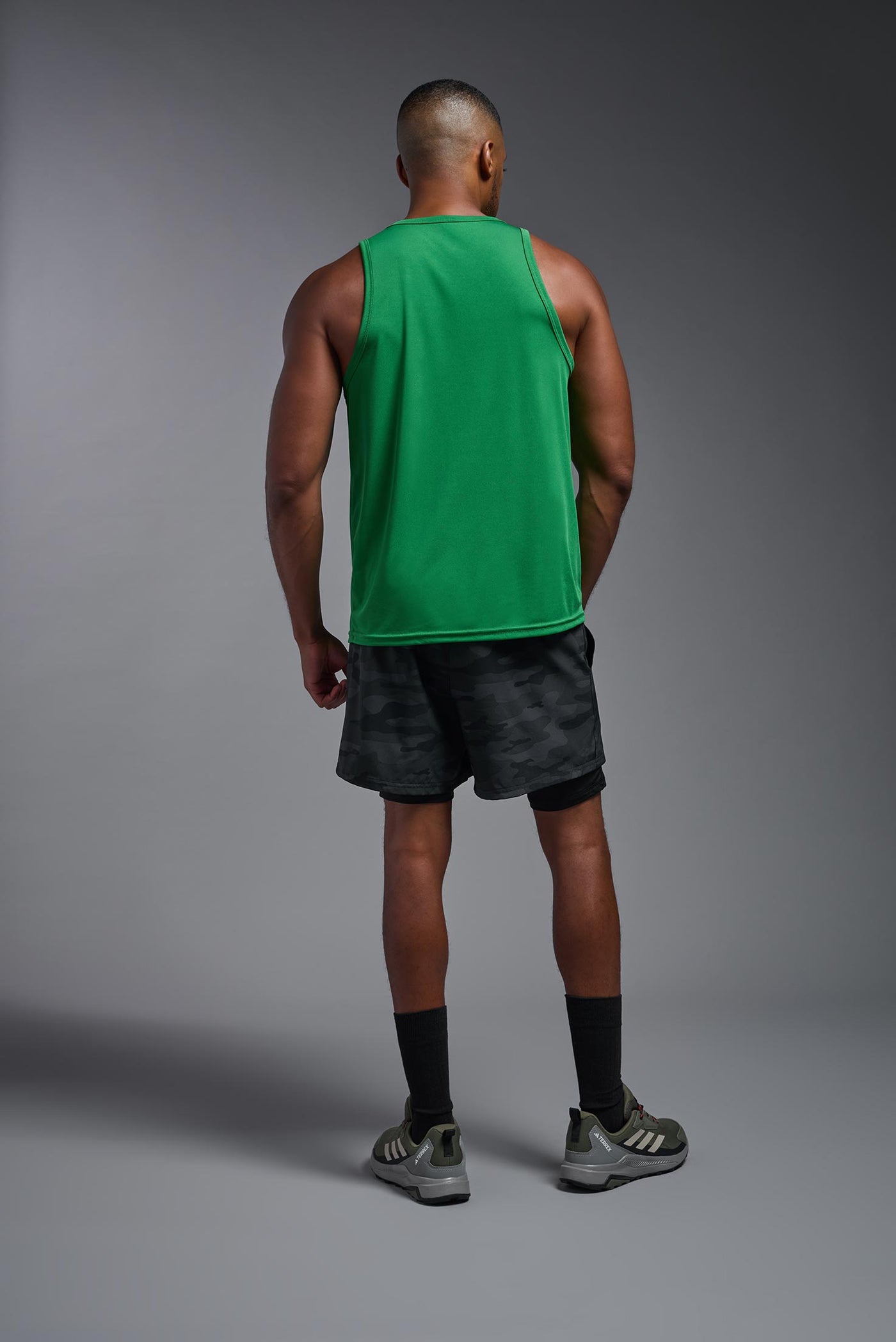 An African American male model with a beard on a gray background, wearing the Men's DriMax Endurance Tank in the color kelly green from a full body back view. This shirt is made in the USA and is quick-drying and moisture-wicking. #color_kelly-green