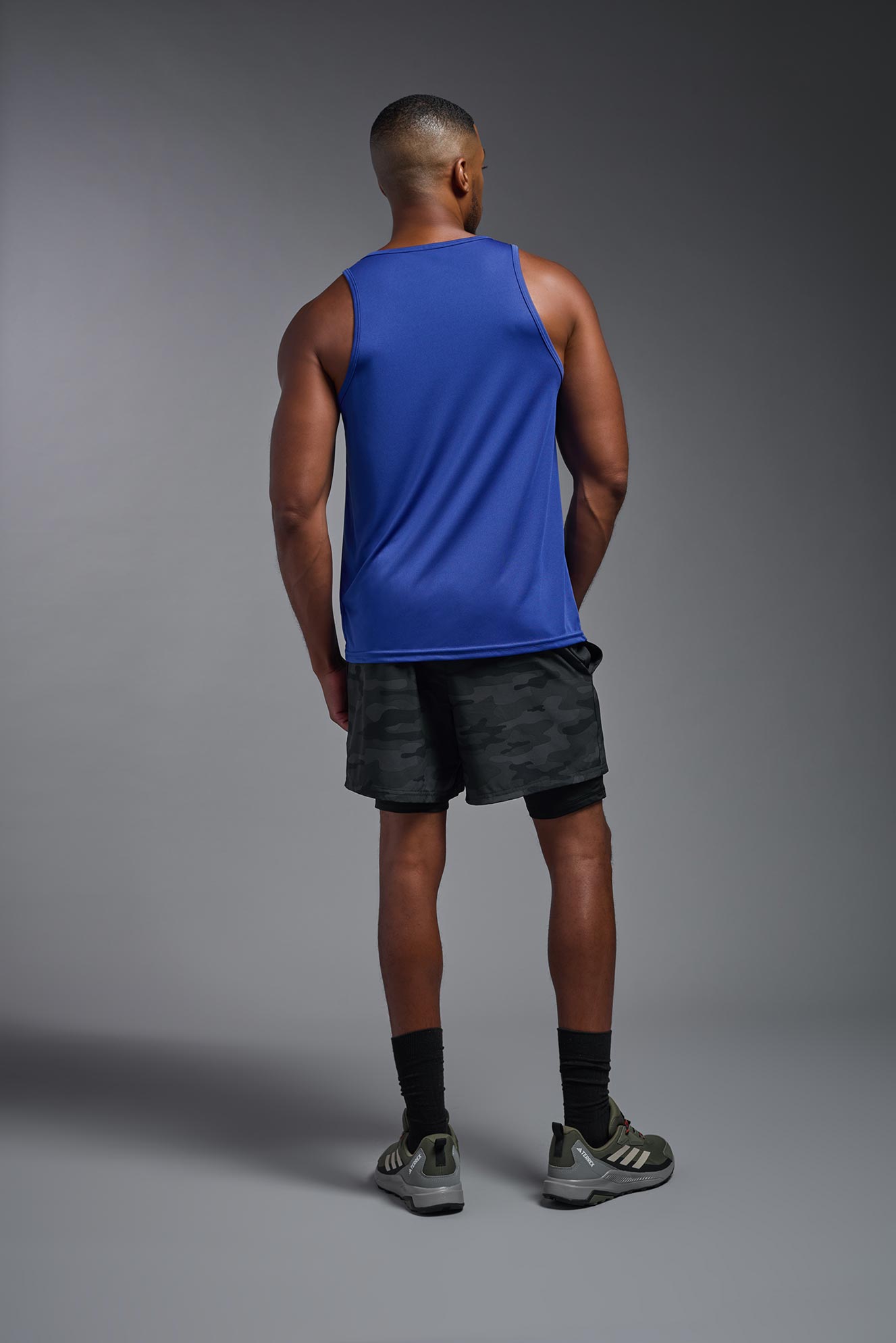 An African American male model with a beard on a gray background, wearing the Men's DriMax Endurance Tank in the color royal blue from a full body back view. This shirt is made in the USA and is quick-drying and moisture-wicking. #color_royal-blue
