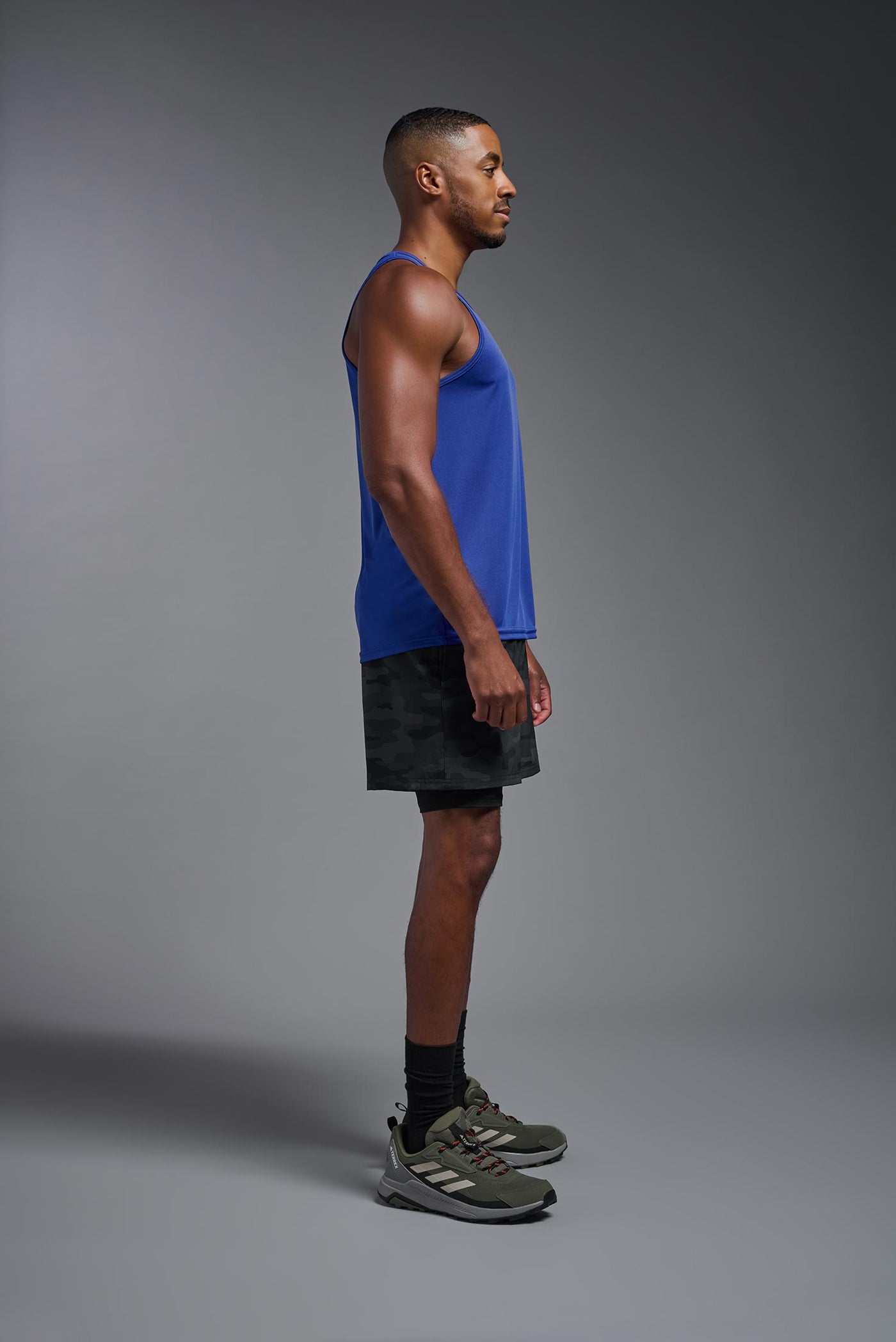 An African American male model with a beard on a gray background, wearing the Men's DriMax Endurance Tank in the color royal blue from a full body side view. This shirt is made in the USA and is quick-drying and moisture-wicking. #color_royal-blue
