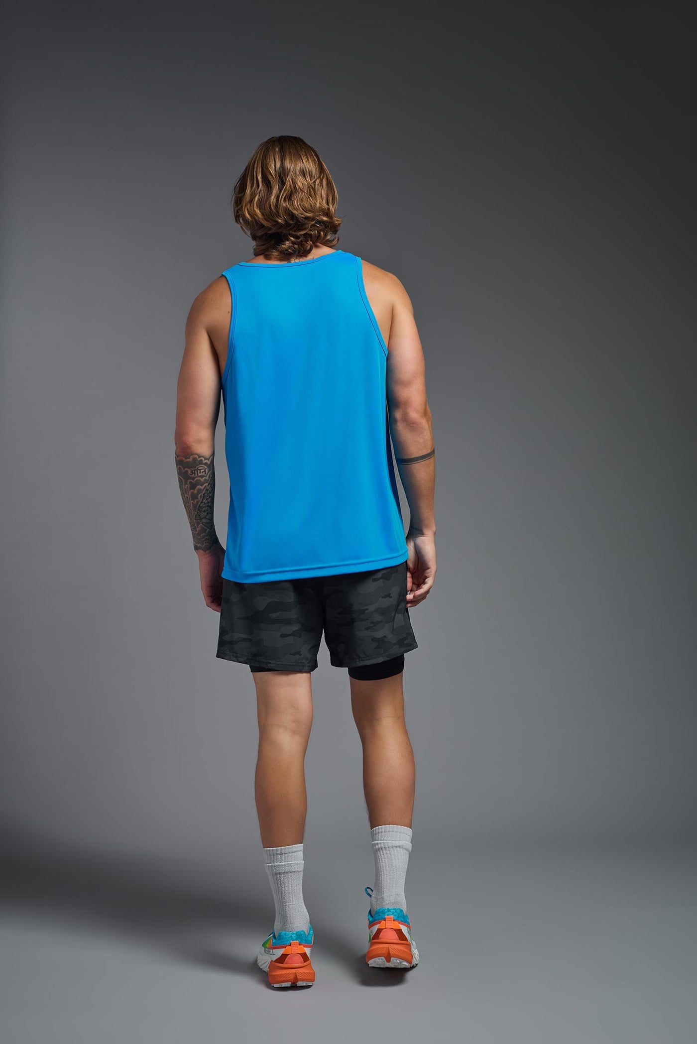 A blonde male model with a beard on a gray background, wearing the Men's DriMax Endurance Tank in the color safety blue from a full body back view. This shirt is made in the USA and is quick-drying and moisture-wicking. #color_safety-blue