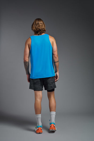 A blonde male model with a beard on a gray background, wearing the Men's DriMax Endurance Tank in the color safety blue from a full body back view. This shirt is made in the USA and is quick-drying and moisture-wicking. #color_safety-blue