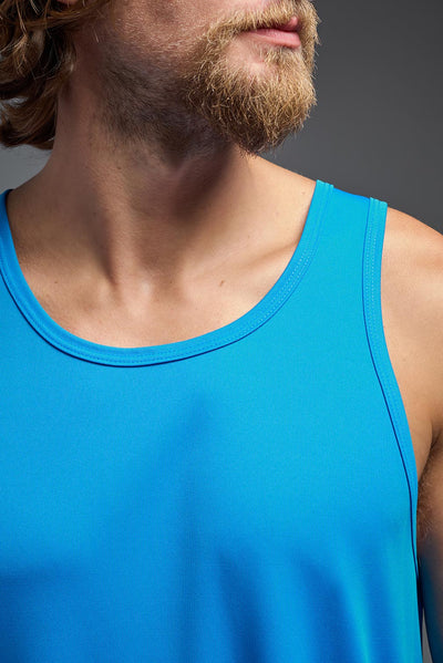 A blonde male model with a beard on a gray background, wearing the Men's DriMax Endurance Tank in the color safety blue from a closeup collar front view. This shirt is made in the USA and is quick-drying and moisture-wicking. #color_safety-blue