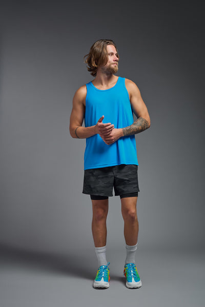 A blonde male model with a beard on a gray background, wearing the Men's DriMax Endurance Tank in the color safety blue from a full body front view. This shirt is made in the USA and is quick-drying and moisture-wicking. #color_safety-blue