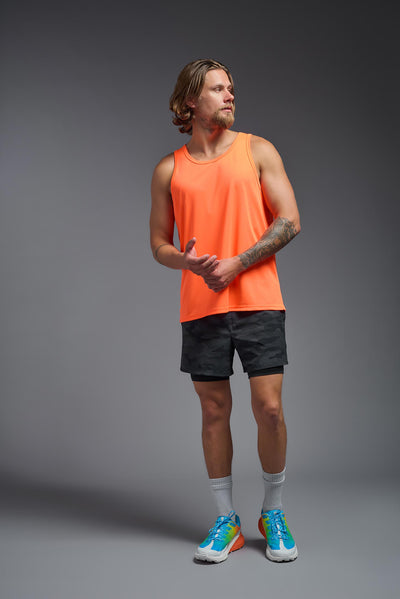 A blonde male model with a beard on a gray background, wearing the Men's DriMax Endurance Tank in the color safety orange from a full body front view. This shirt is made in the USA and is quick-drying and moisture-wicking. #color_safety-orange