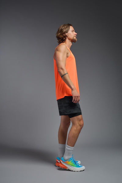 A blonde male model with a beard on a gray background, wearing the Men's DriMax Endurance Tank in the color safety orange from a full body side view. This shirt is made in the USA and is quick-drying and moisture-wicking. #color_safety-orange