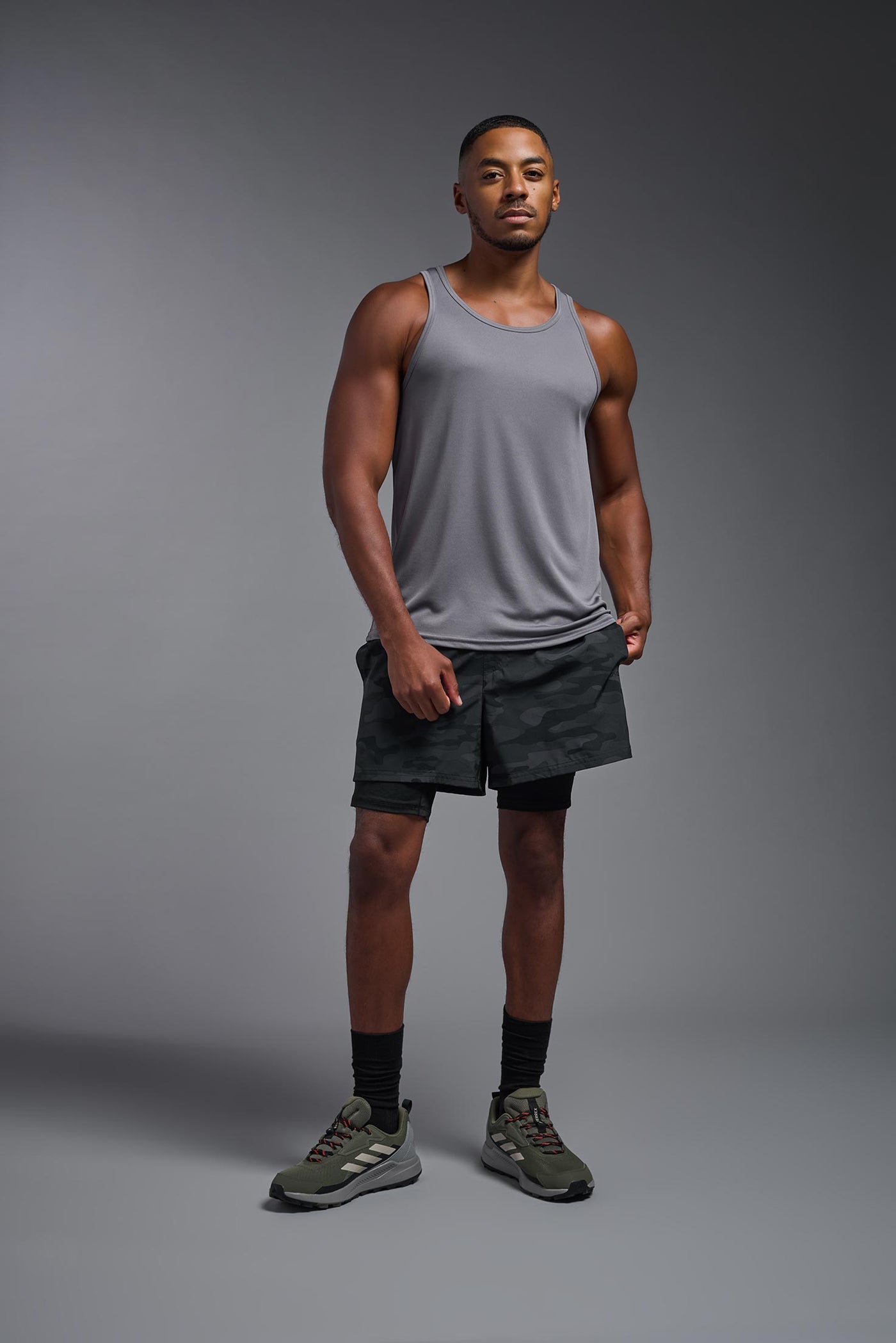 An African American male model with a beard on a gray background, wearing the Men's DriMax Endurance Tank in the color steel gray from a full body front view. This shirt is made in the USA and is quick-drying and moisture-wicking. #color_steel