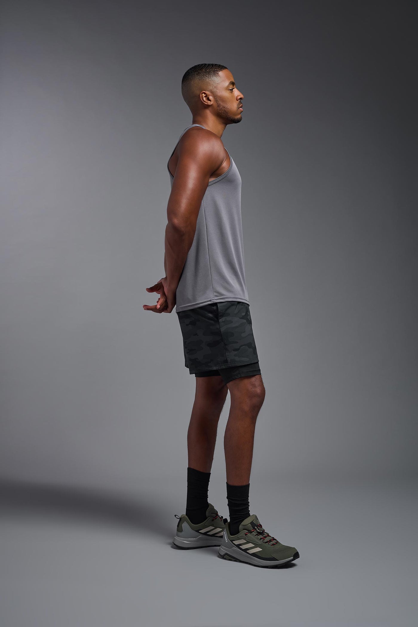 An African American male model with a beard on a gray background, wearing the Men's DriMax Endurance Tank in the color steel gray from a full body side view. This shirt is made in the USA and is quick-drying and moisture-wicking. #color_steel