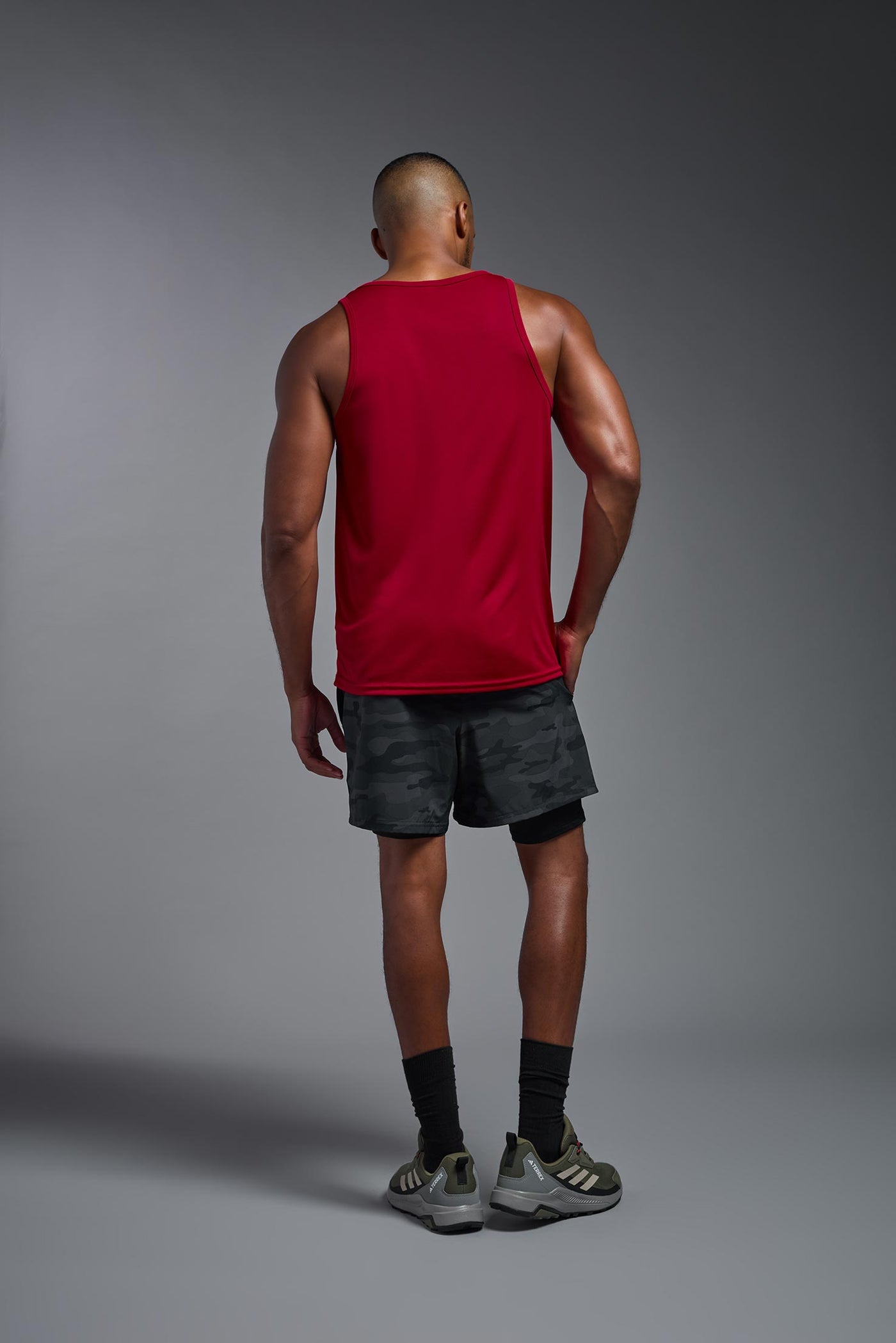 An African American male model with a beard on a gray background, wearing the Men's DriMax Endurance Tank in the color true red from a full body back view. This shirt is made in the USA and is quick-drying and moisture-wicking. #color_true-red