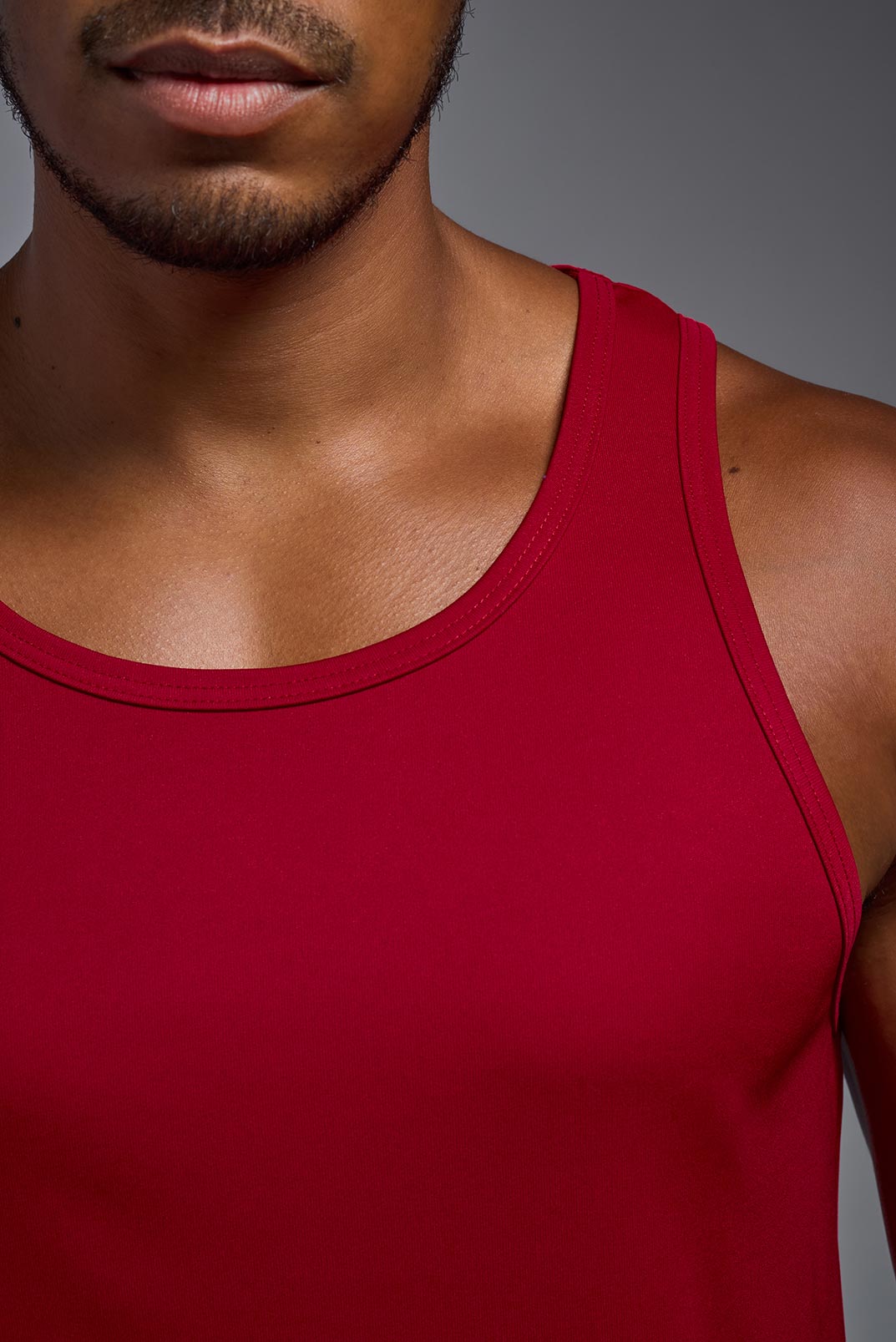 An African American male model with a beard on a gray background, wearing the Men's DriMax Endurance Tank in the color true red from a full body collar view. This shirt is made in the USA and is quick-drying and moisture-wicking. #color_true-red