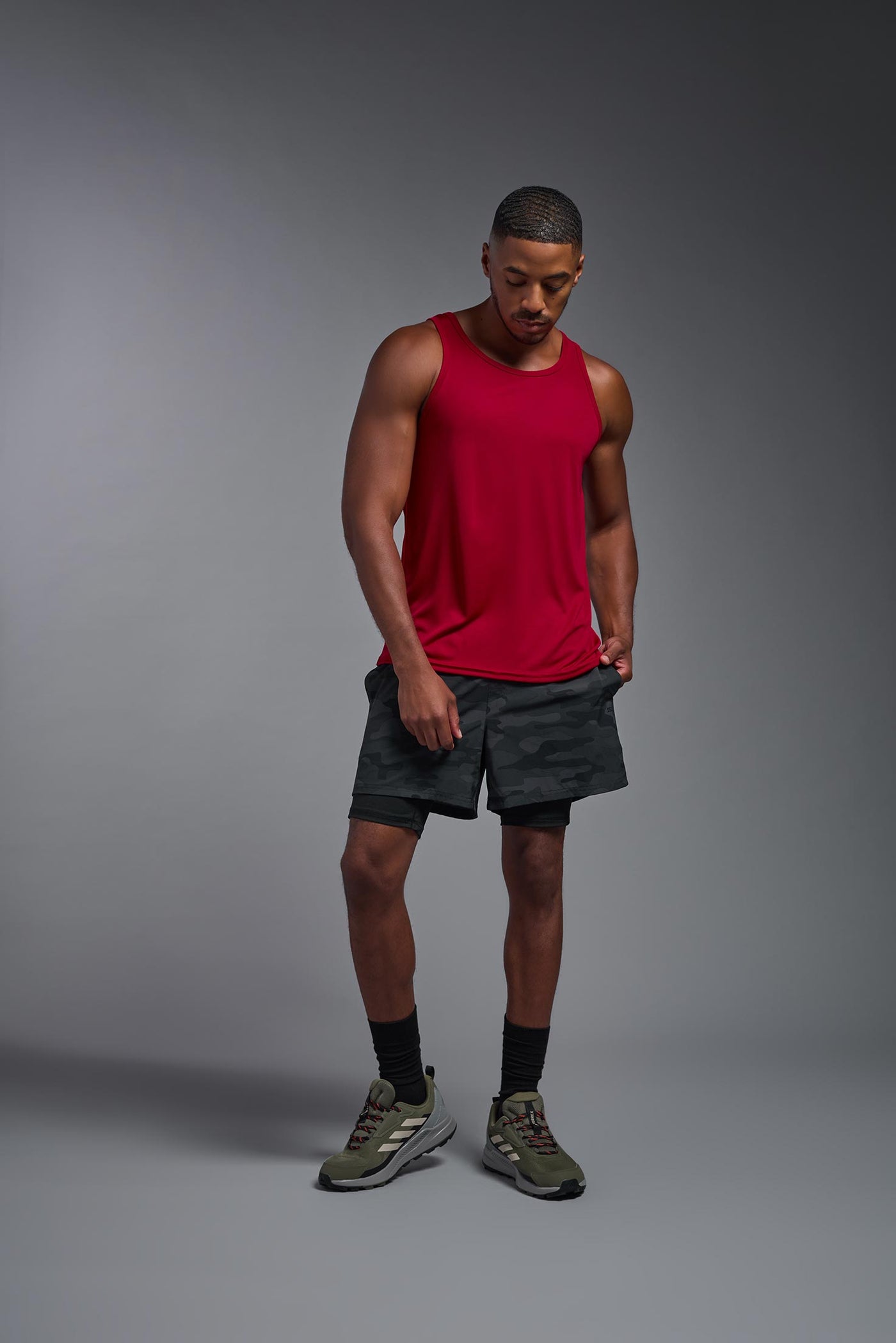 An African American male model with a beard on a gray background, wearing the Men's DriMax Endurance Tank in the color true red from a full body front view. This shirt is made in the USA and is quick-drying and moisture-wicking. #color_true-red