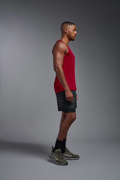An African American male model with a beard on a gray background, wearing the Men's DriMax Endurance Tank in the color true red from a full body side view. This shirt is made in the USA and is quick-drying and moisture-wicking. #color_true-red