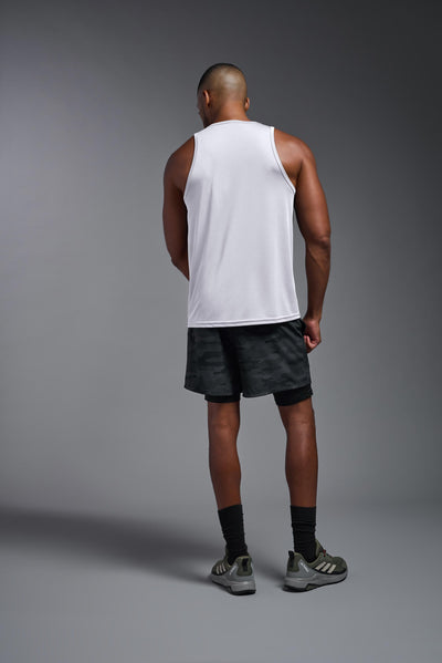 A blonde male model with a beard on a gray background, wearing the Men's DriMax Endurance Tank in the color white from a full body back view. This shirt is made in the USA and is quick-drying and moisture-wicking. #color_white