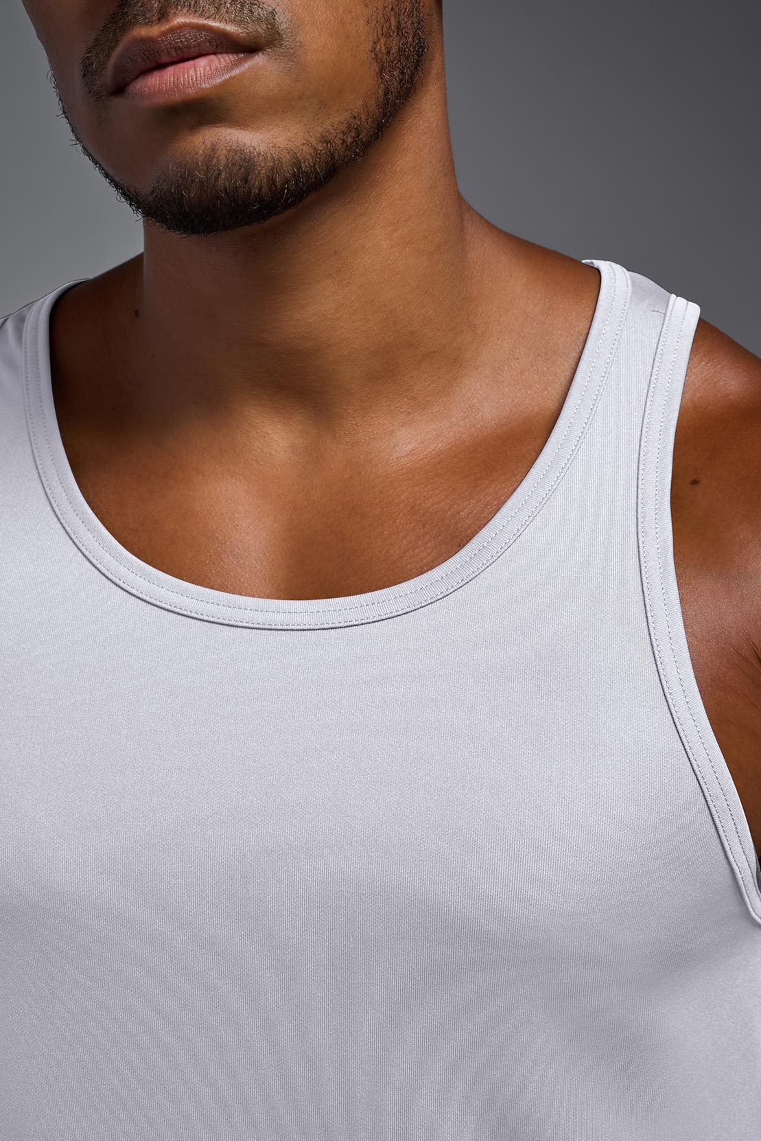 A blonde male model with a beard on a gray background, wearing the Men's DriMax Endurance from a closeup collar view. This shirt is made in the USA and is quick-drying and moisture-wicking. #color_white