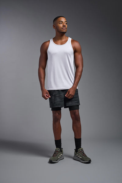 A blonde male model with a beard on a gray background, wearing the Men's DriMax Endurance Tank in the color white from a full body front view. This shirt is made in the USA and is quick-drying and moisture-wicking. #color_white