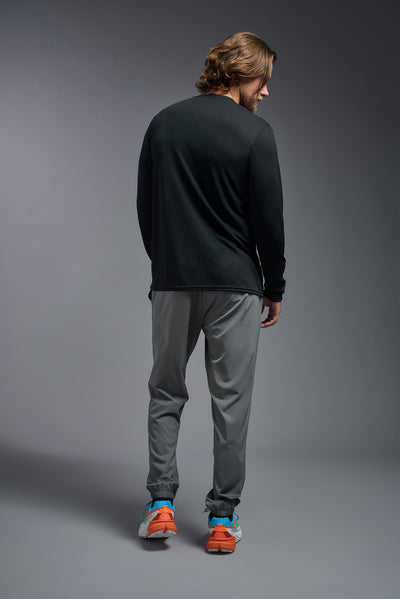 A blonde male model with a beard on a gray background, wearing the Men's DriMax Long Sleeve Expert Shirt in the color black from a full body back view. This shirt is made in the USA and is quick-drying and moisture-wicking. #color_black