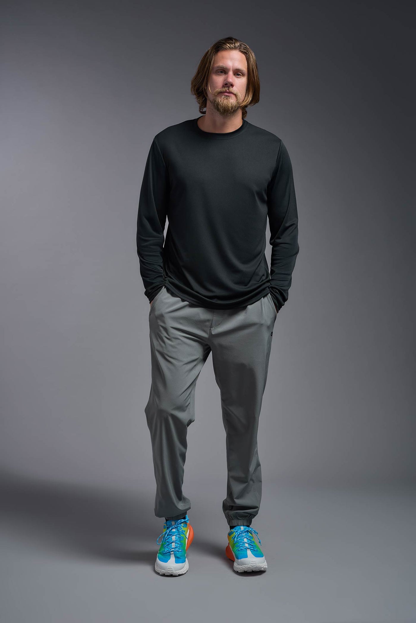 A blonde male model with a beard on a gray background, wearing the Men's DriMax Long Sleeve Expert Shirt in the color black from a full body front view. This shirt is made in the USA and is quick-drying and moisture-wicking. #color_black
