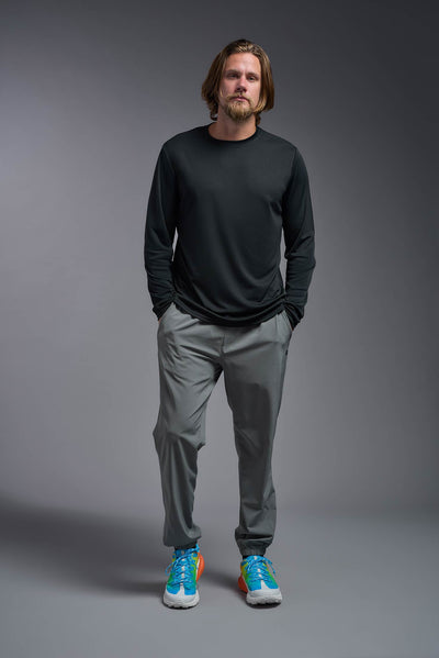 A blonde male model with a beard on a gray background, wearing the Men's DriMax Long Sleeve Expert Shirt in the color black from a full body front view. This shirt is made in the USA and is quick-drying and moisture-wicking. #color_black