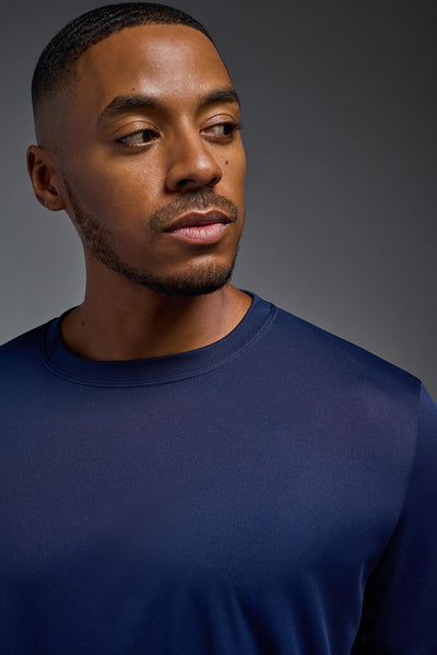 An African American male model with a beard on a gray background, wearing the Men's DriMax Long Sleeve Expert Shirt in the color navy from a close-up collar view. This shirt is made in the USA and is quick-drying and moisture-wicking. #color_navy