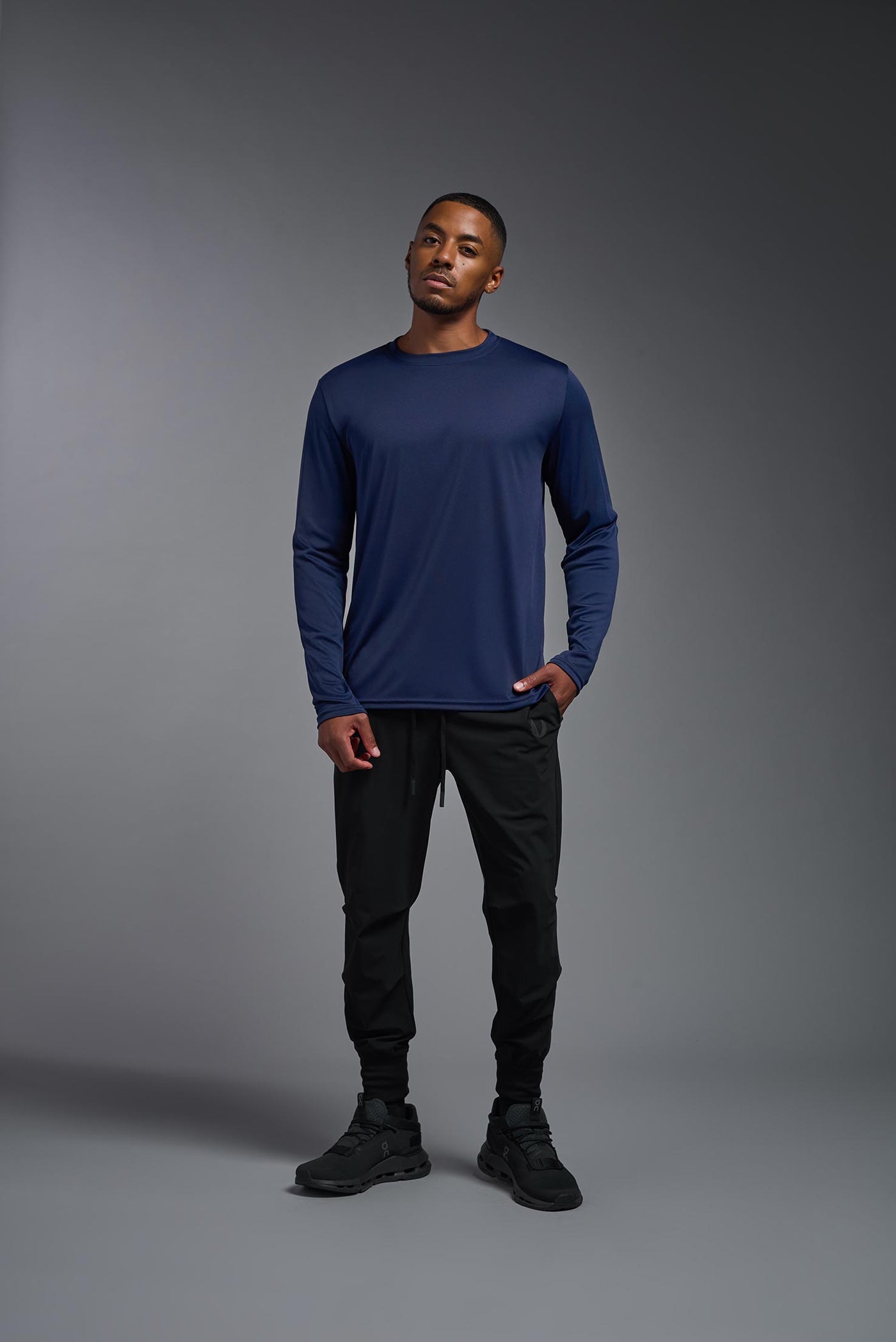 An African American male model with a beard on a gray background, wearing the Men's DriMax Long Sleeve Expert Shirt in the color navy from a full body front view. This shirt is made in the USA and is quick-drying and moisture-wicking. #color_navy