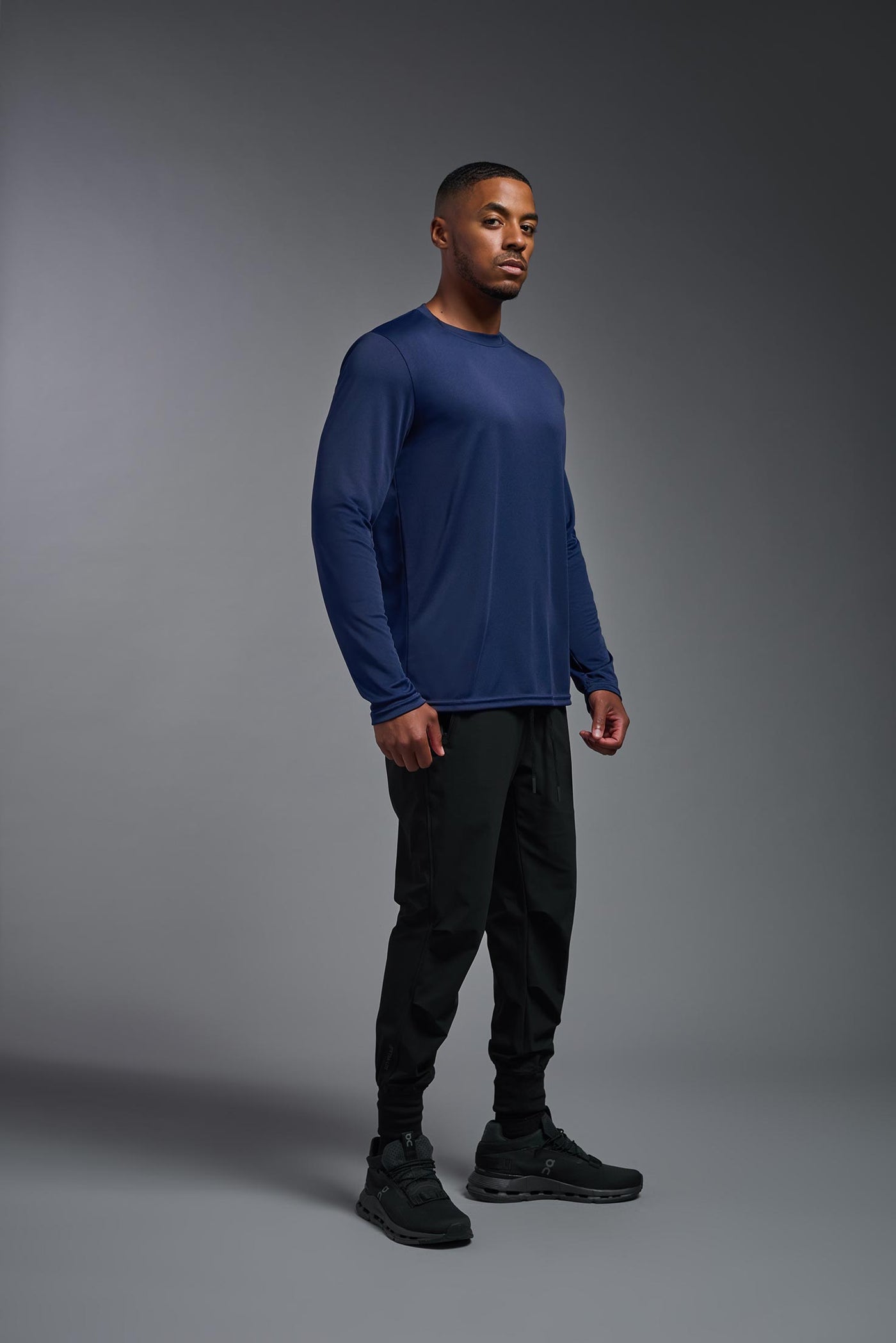 An African American male model with a beard on a gray background, wearing the Men's DriMax Long Sleeve Expert Shirt in the color navy from a full body side view. This shirt is made in the USA and is quick-drying and moisture-wicking. #color_navy