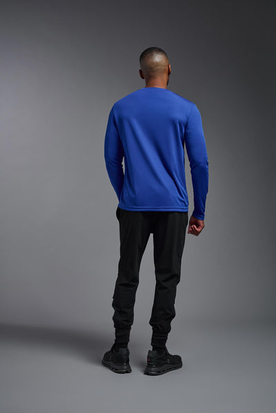 An African American male model with a beard on a gray background, wearing the Men's DriMax Long Sleeve Expert Shirt in the color royal blue from a full body side view. This shirt is made in the USA and is quick-drying and moisture-wicking. #color_royal-blue