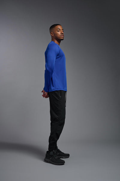 An African American male model with a beard on a gray background, wearing the Men's DriMax Long Sleeve Expert Shirt in the color royal blue from a full body side view. This shirt is made in the USA and is quick-drying and moisture-wicking. #color_royal-blue
