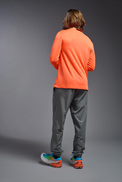 A blonde male model with a beard on a gray background, wearing the Men's DriMax Long Sleeve Expert Shirt in the color safety orange from a full body back view. This shirt is made in the USA and is quick-drying and moisture-wicking. #color_safety-orange