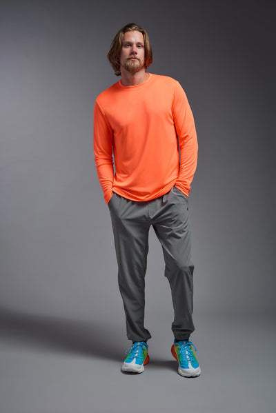 A blonde male model with a beard on a gray background, wearing the Men's DriMax Long Sleeve Expert Shirt in the color safety orange from a full body front view. This shirt is made in the USA and is quick-drying and moisture-wicking. #color_safety-orange