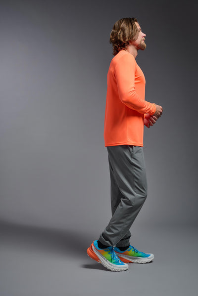 A blonde male model with a beard on a gray background, wearing the Men's DriMax Long Sleeve Expert Shirt in the color safety orange from a full body side view. This shirt is made in the USA and is quick-drying and moisture-wicking. #color_safety-orange