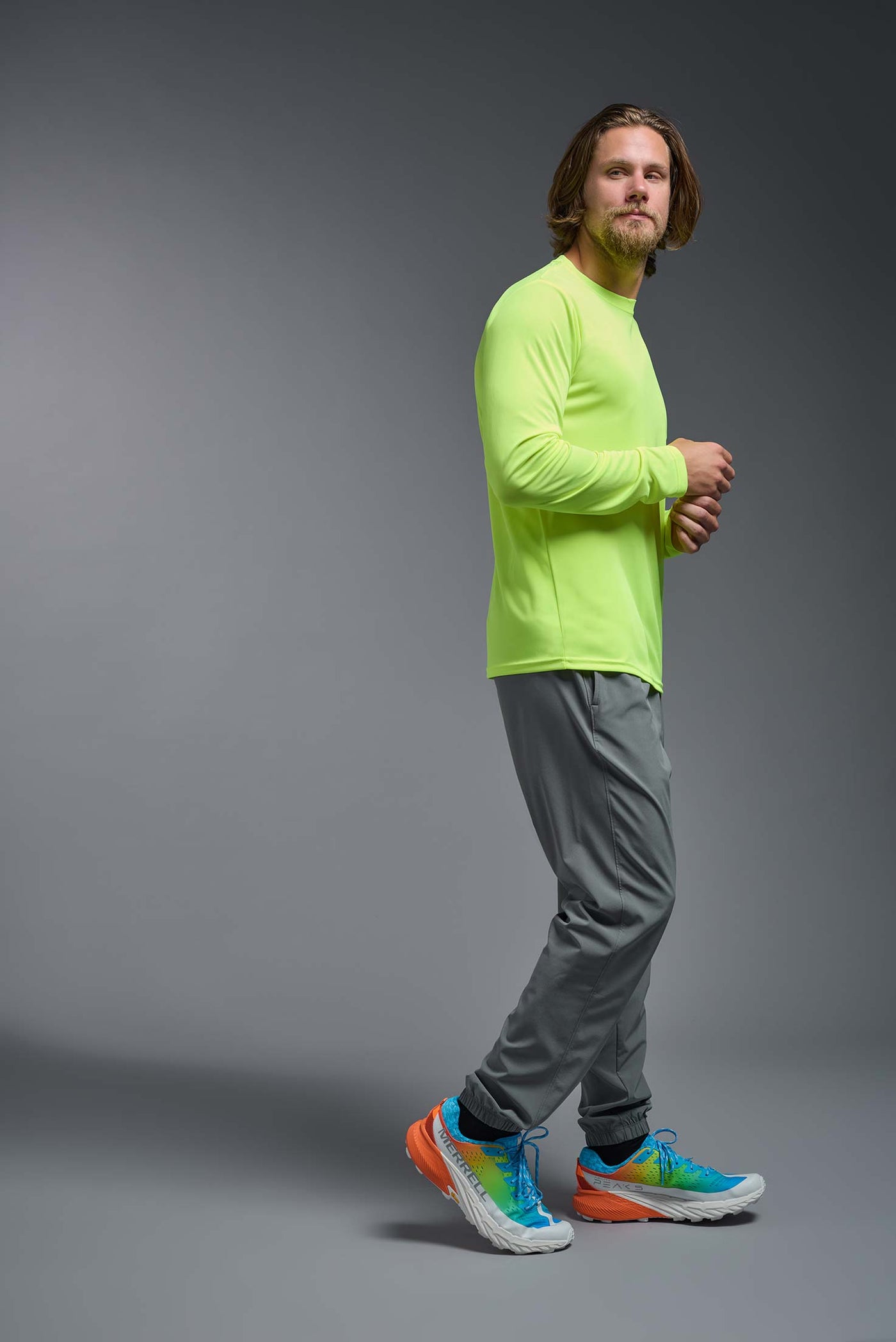 An African American male model with a beard on a gray background, wearing the Men's DriMax Long Sleeve Expert Shirt in the color safety yellow from a full body side view. This shirt is made in the USA and is quick-drying and moisture-wicking. #color_safety-yellow