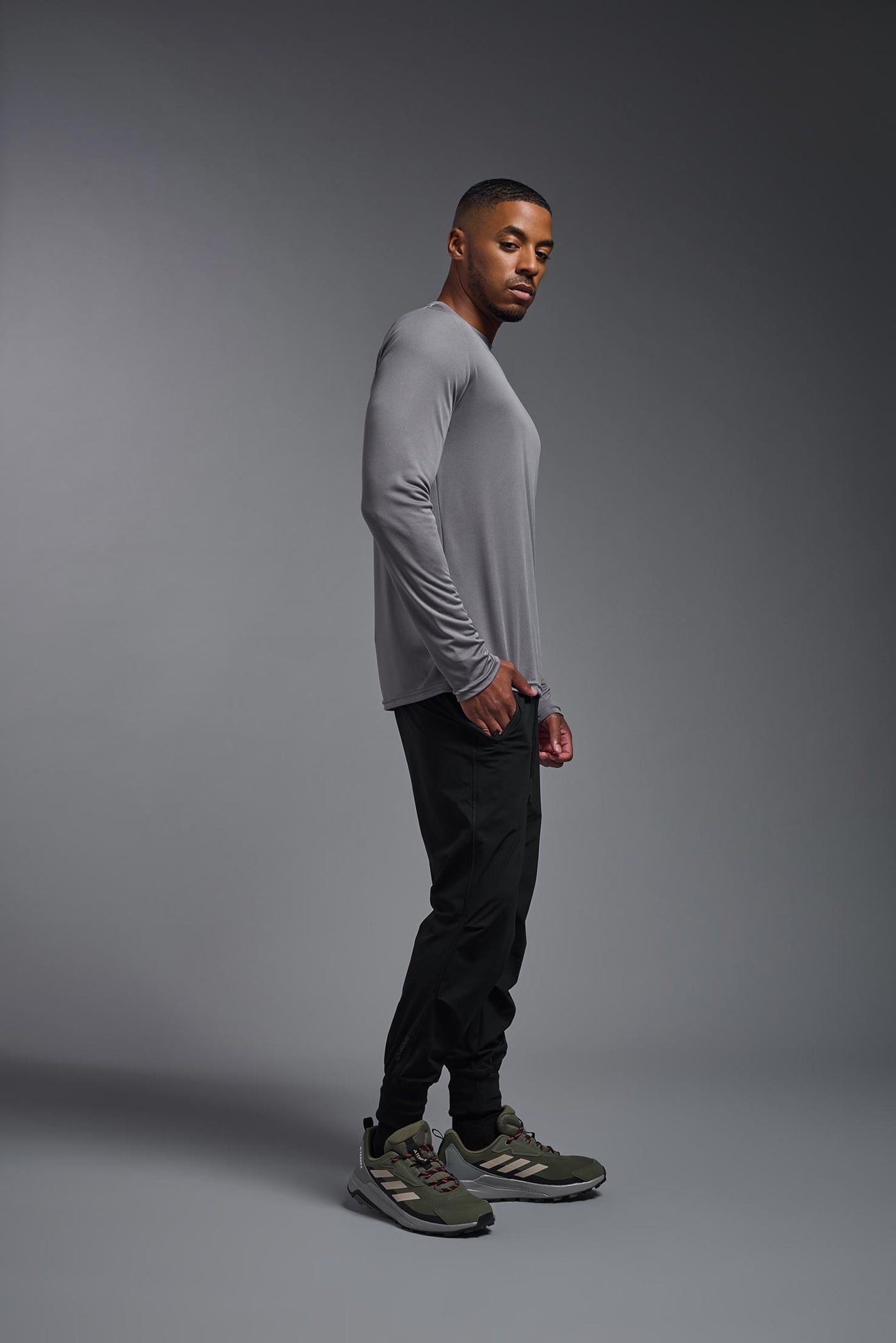 An African American male model with a beard on a gray background, wearing the Men's DriMax Long Sleeve Expert Shirt in the color steel from a full body side view. This shirt is made in the USA and is quick-drying and moisture-wicking. #color_steel
