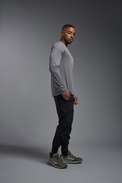 An African American male model with a beard on a gray background, wearing the Men's DriMax Long Sleeve Expert Shirt in the color steel from a full body side view. This shirt is made in the USA and is quick-drying and moisture-wicking. #color_steel