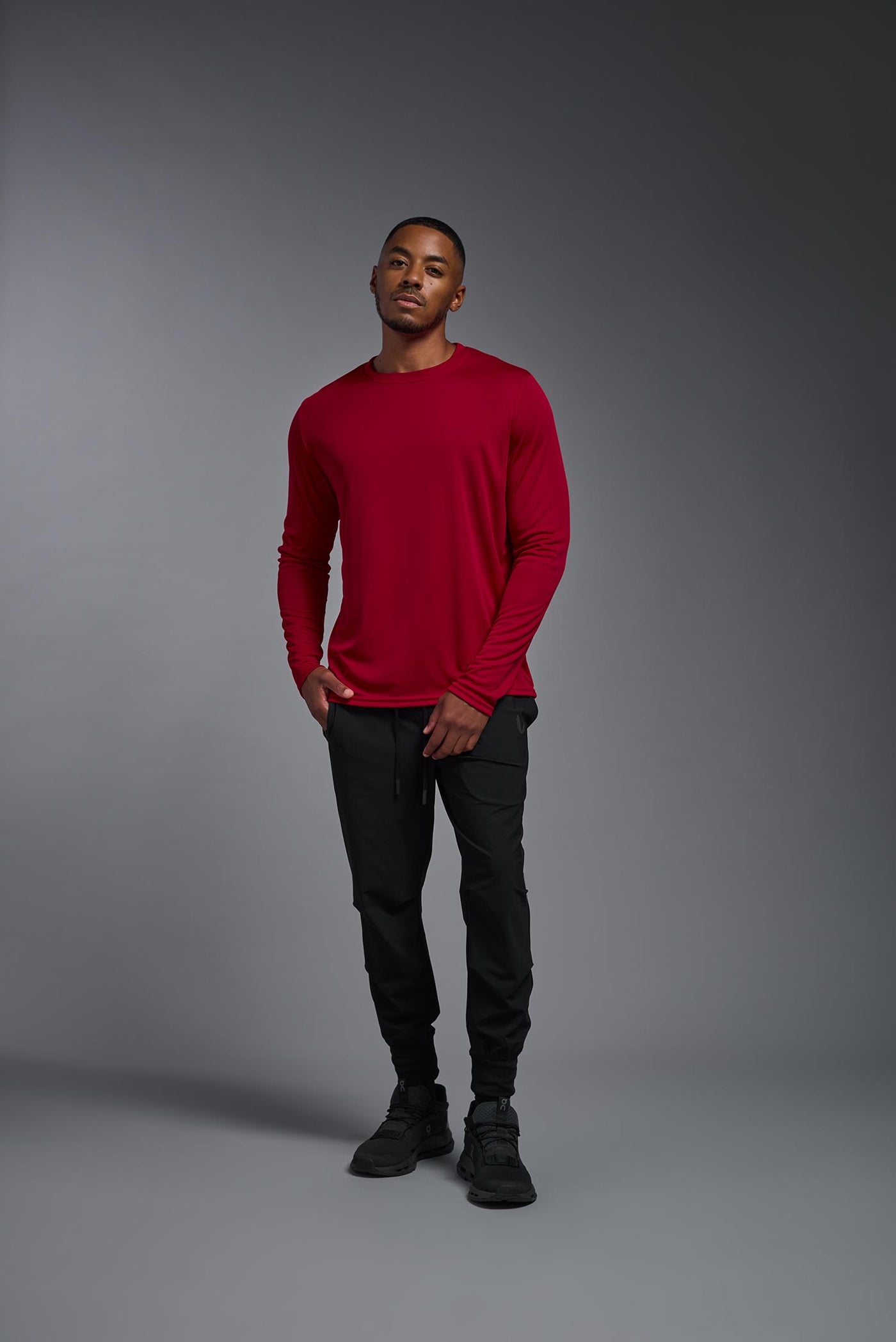 An African American male model with a beard on a gray background, wearing the Men's DriMax Long Sleeve Expert Shirt in the color true red from a full body front view. This shirt is made in the USA and is quick-drying and moisture-wicking. #color_true-red
