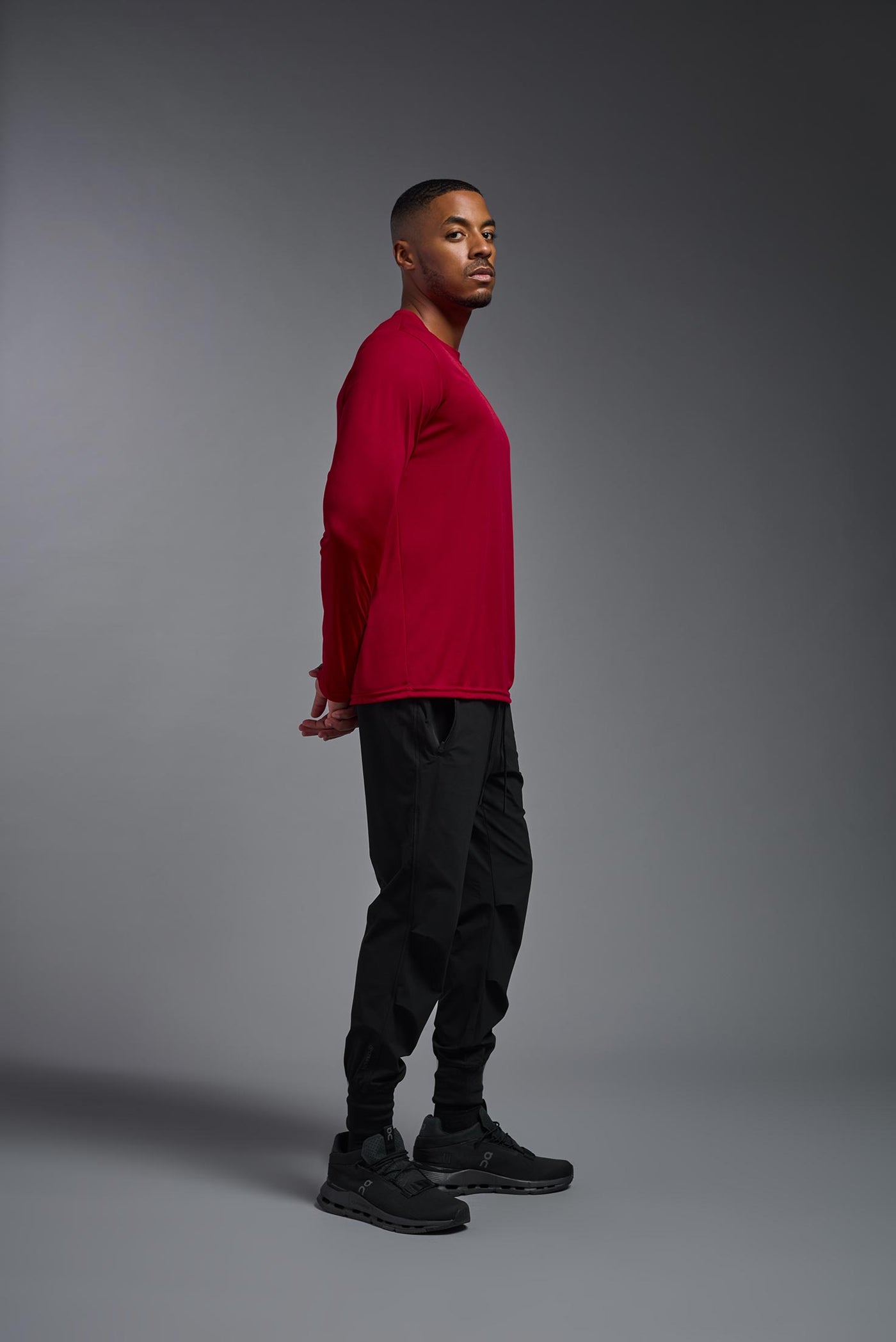 An African American male model with a beard on a gray background, wearing the Men's DriMax Long Sleeve Expert Shirt in the color true red from a full body side view. This shirt is made in the USA and is quick-drying and moisture-wicking. #color_true-red