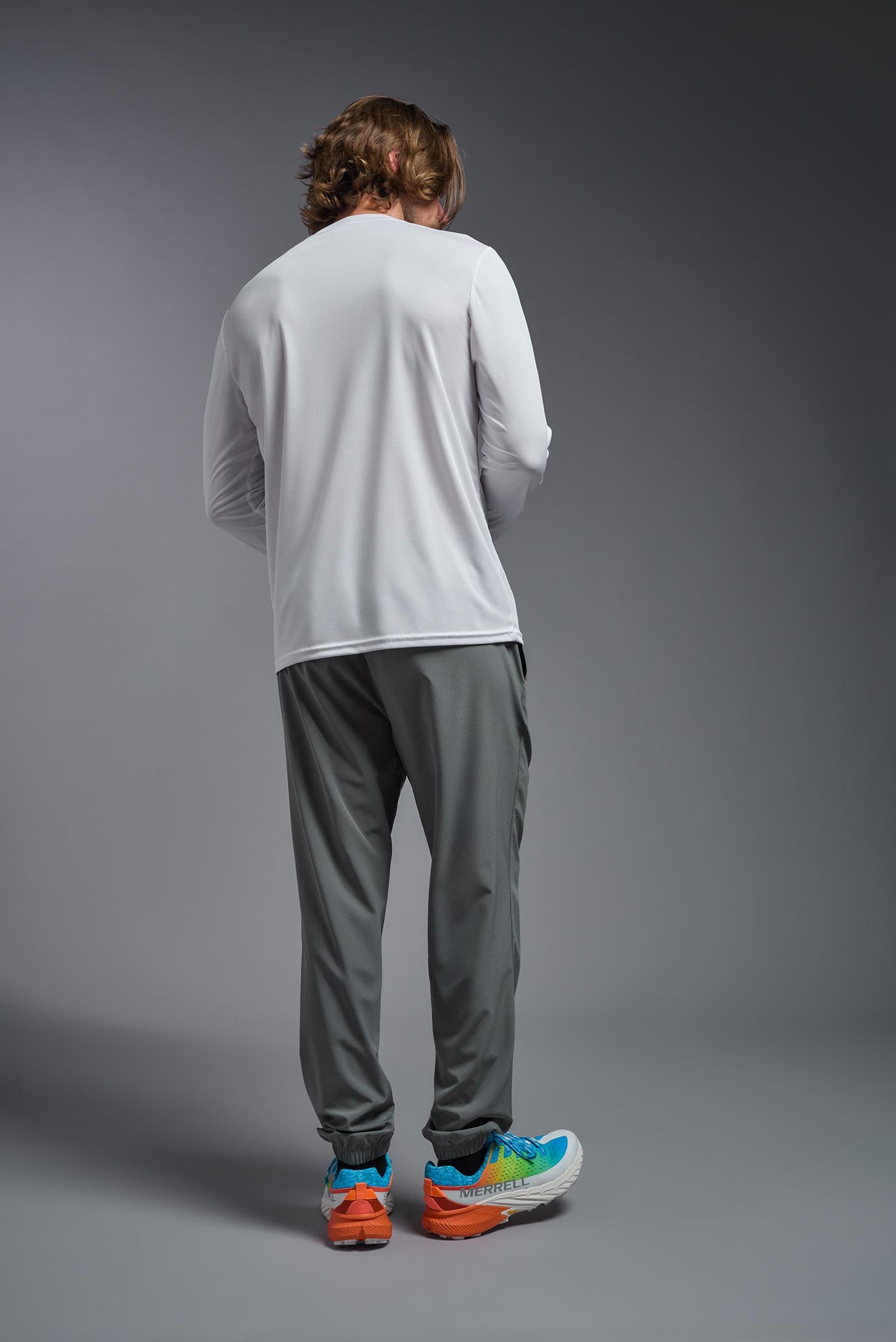 A blonde male model with a beard on a gray background, wearing the Men's DriMax Long Sleeve Expert Shirt in the color white from a full body back view. This shirt is made in the USA and is quick-drying and moisture-wicking. #color_white