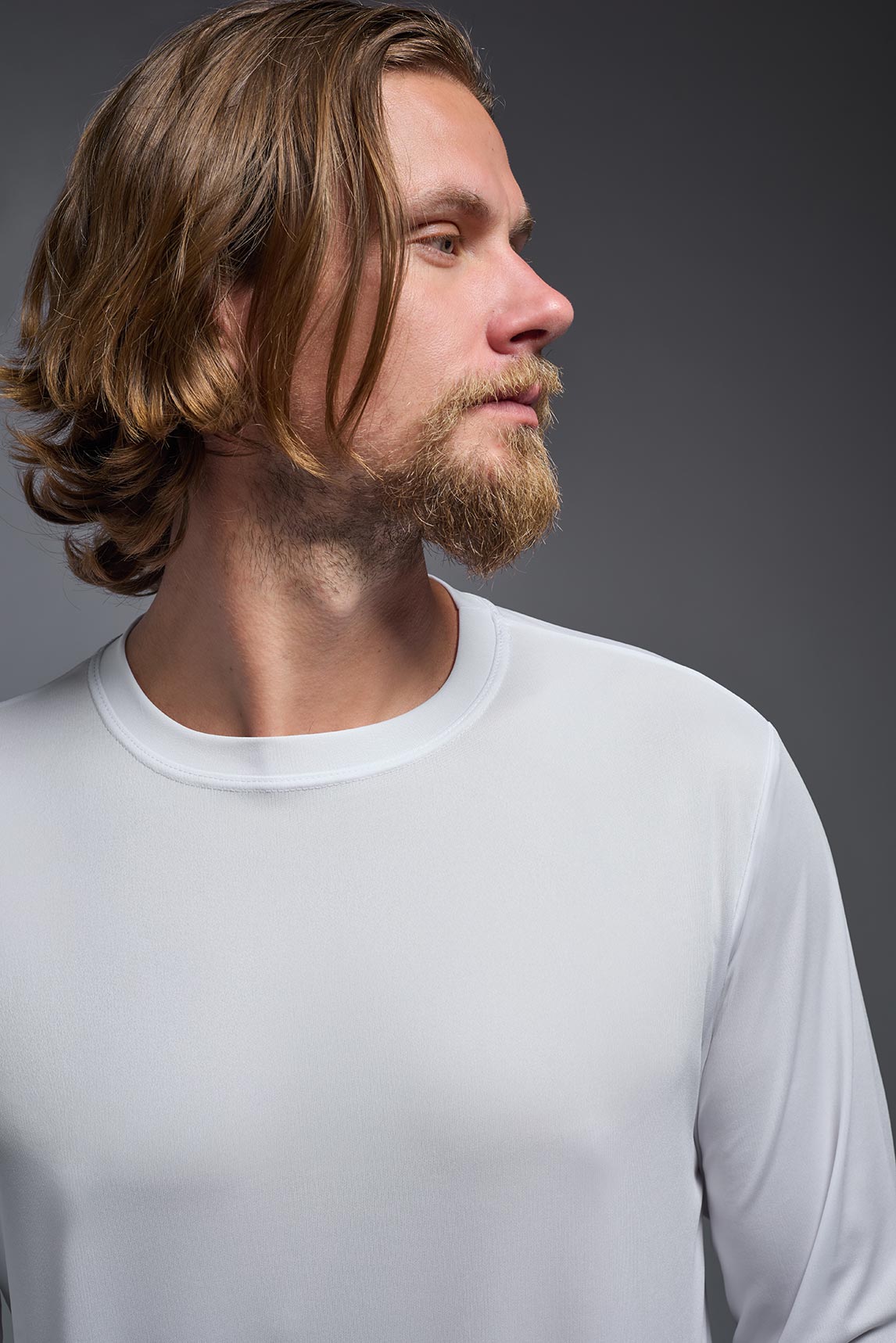 A blonde male model with a beard on a gray background, wearing the Men's DriMax Long Sleeve Expert Shirt in the color white from a close-up collar view. This shirt is made in the USA and is quick-drying and moisture-wicking. #color_white