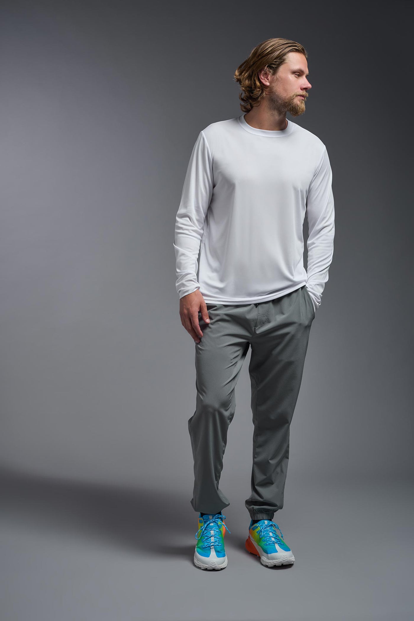 A blonde male model with a beard on a gray background, wearing the Men's DriMax Long Sleeve Expert Shirt in the color white from a full body front view. This shirt is made in the USA and is quick-drying and moisture-wicking. #color_white