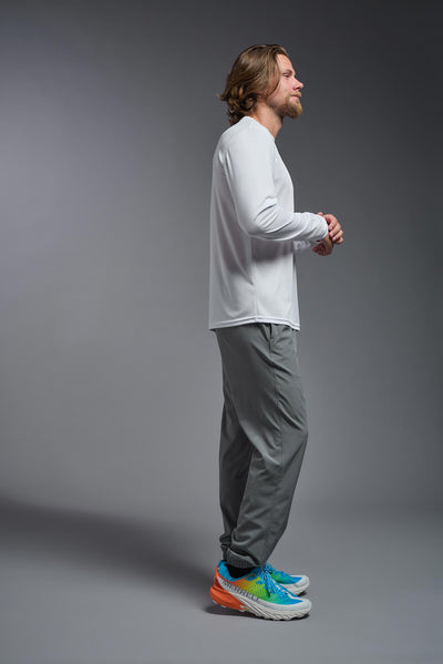 A blonde male model with a beard on a gray background, wearing the Men's DriMax Long Sleeve Expert Shirt in the color white from a full body side view. This shirt is made in the USA and is quick-drying and moisture-wicking. #color_white