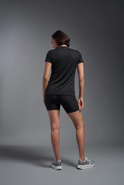 A female model with brown short hair on a gray background, wearing the Women's Oxymesh™ V-neck Tech Tee in the color black from a full body back view. This shirt is made in the USA and is quick-drying and moisture-wicking. #color_black