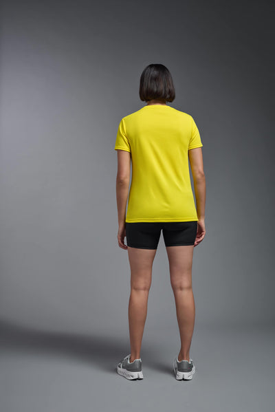 A female model with brown short hair on a gray background, wearing the Women's Oxymesh™ V-neck Tech Tee in the color bright yellow from a full body back view. This shirt is made in the USA and is quick-drying and moisture-wicking. #color_bright-yellow