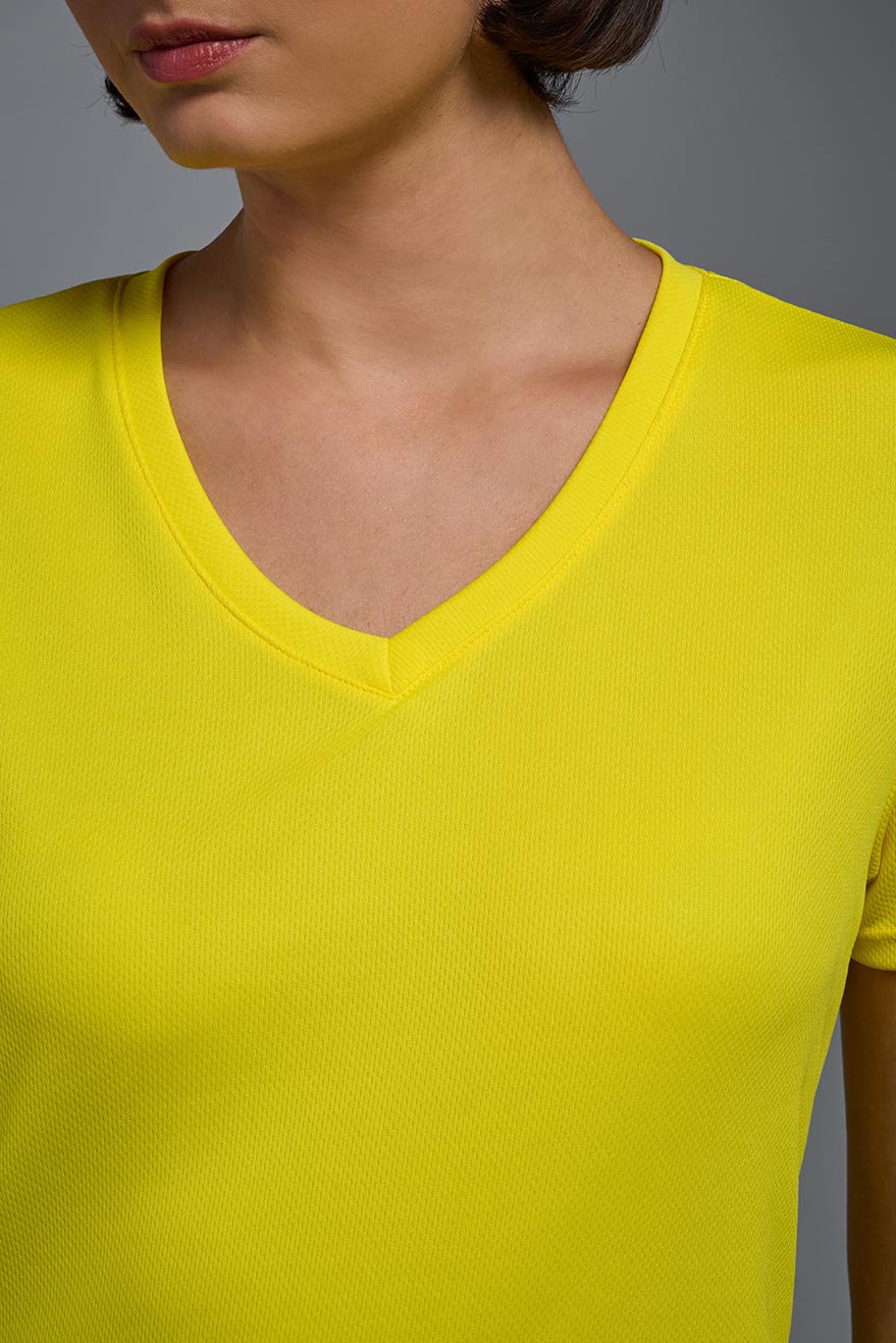 A female model with brown short hair on a gray background, wearing the Women's Oxymesh™ V-neck Tech Tee in the color bright yellow from a closeup collar front view. This shirt is made in the USA and is quick-drying and moisture-wicking. #color_bright-yellow
