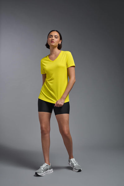 A female model with brown short hair on a gray background, wearing the Women's Oxymesh™ V-neck Tech Tee in the color bright yellow from a full body front view. This shirt is made in the USA and is quick-drying and moisture-wicking. #color_bright-yellow