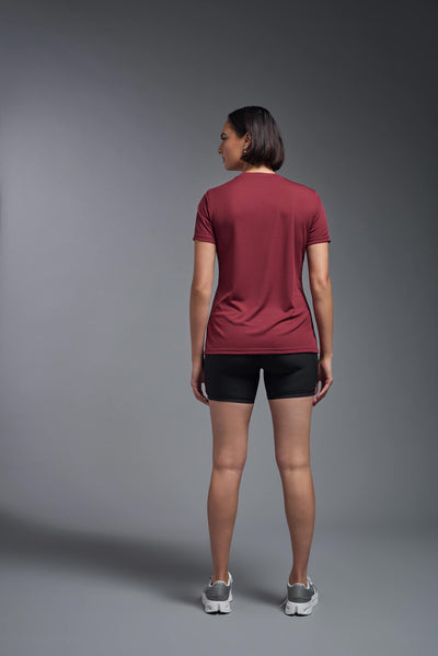 A female model with brown short hair on a gray background, wearing the Women's Oxymesh™ V-neck Tech Tee in the color cardinal from a full body back view. This shirt is made in the USA and is quick-drying and moisture-wicking. #color_cardinal