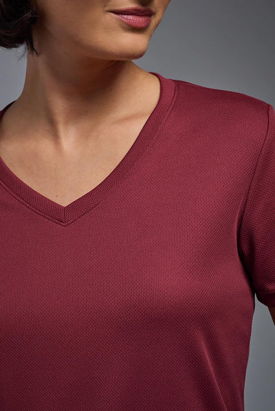 A female model with brown short hair on a gray background, wearing the Women's Oxymesh™ V-neck Tech Tee in the color cardinal from a closeup collar front view. This shirt is made in the USA and is quick-drying and moisture-wicking. #color_cardinal