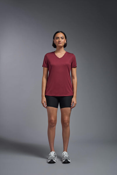 A female model with brown short hair on a gray background, wearing the Women's Oxymesh™ V-neck Tech Tee in the color cardinal from a full body front view. This shirt is made in the USA and is quick-drying and moisture-wicking. #color_cardinal